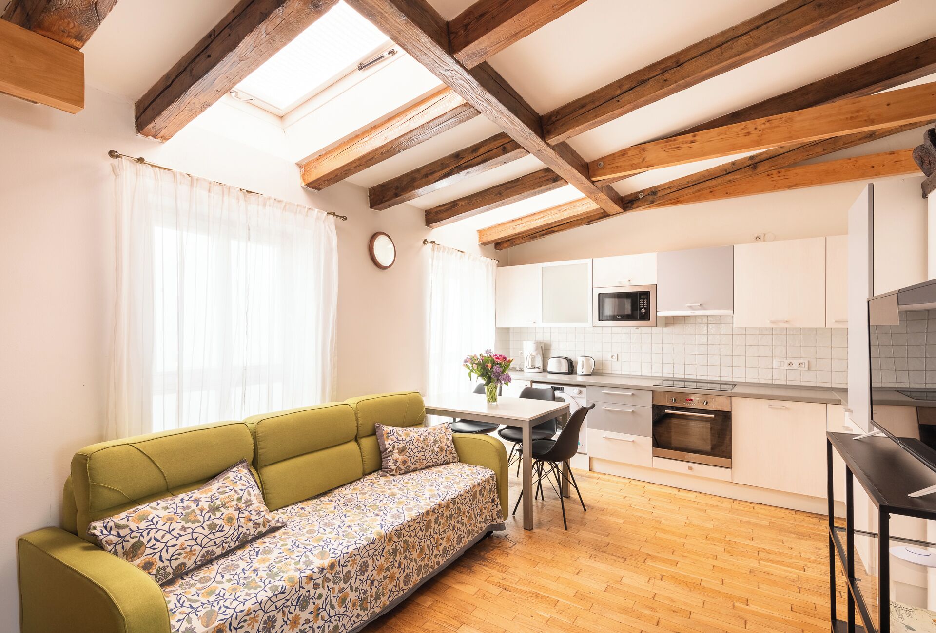 A cozy living room with a sofa, a dining area with a table and chairs, and a kitchen with white cabinets and appliances.