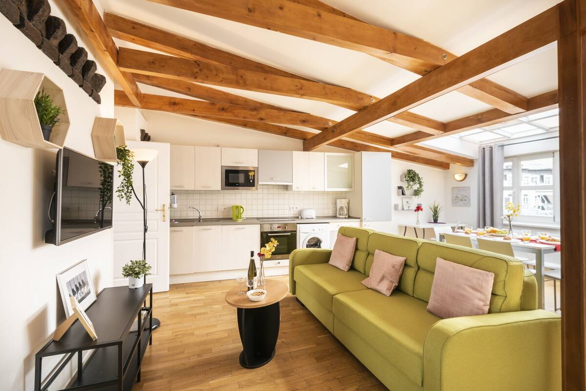 A modern kitchen with white cabinets, a microwave, and a dining area with a green sofa and a table.