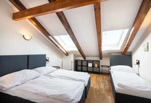 Quarto com duas camas, vigas de madeira, claraboias, um radiador e uma pequena mesa.