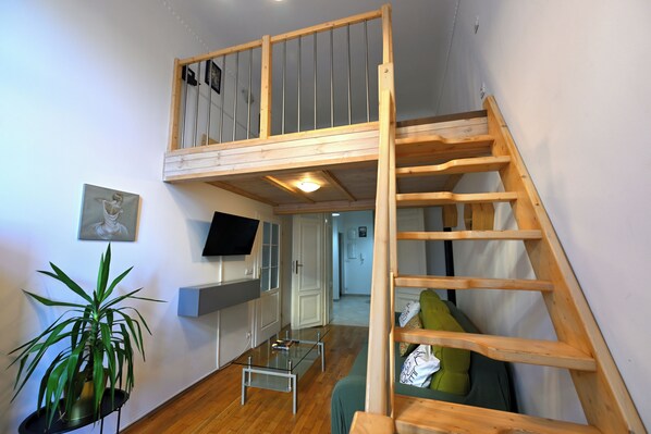 A loft-style room with a wooden staircase, a flat-screen TV mounted on the wall, a green sofa, and a potted plant. - Hybernska Apartments (Prague)