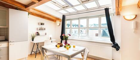 A modern kitchen with a dining area, wooden beams, a skylight, and a view of the city.