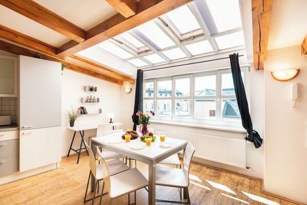 A modern kitchen with a dining area, wooden beams, a skylight, and a view of the city. - Hybernska Apartments (Prague)