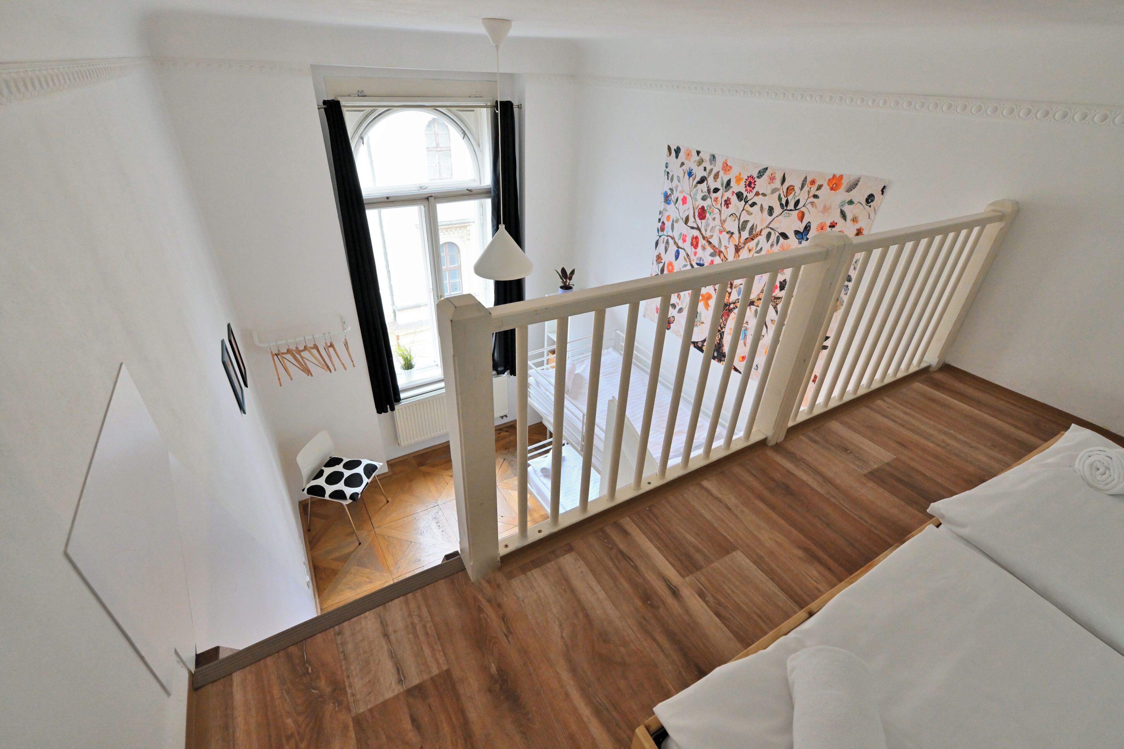 Een kamer met een houten vloer, een wit bed, een witte balustrade, een raam met uitzicht en een deur die naar buiten leidt.