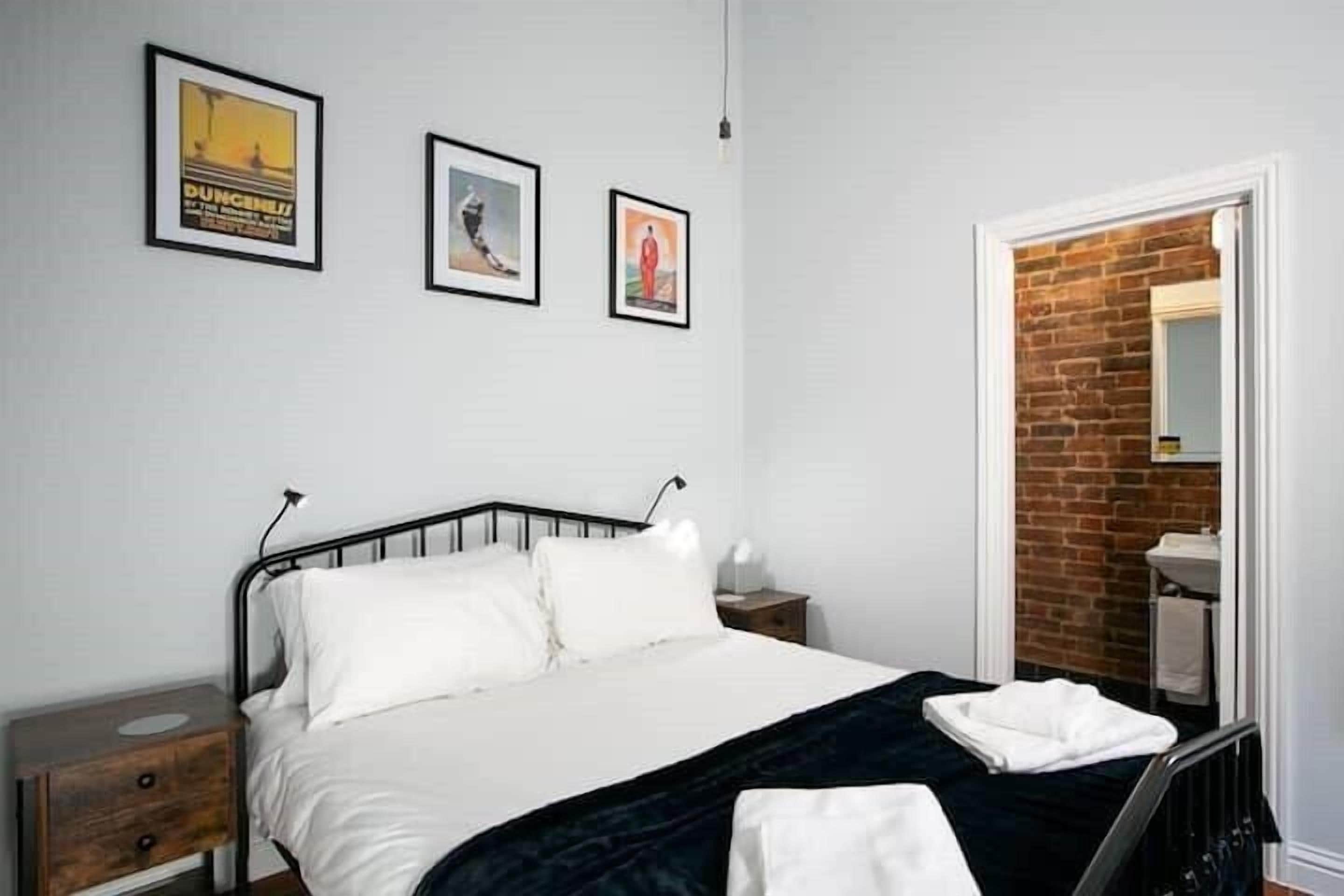 Une chambre à coucher avec un lit, une table de chevet, une commode et un mur en briques.