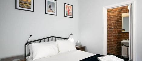 Une chambre à coucher avec un lit, une table de chevet, une commode et un mur en briques.