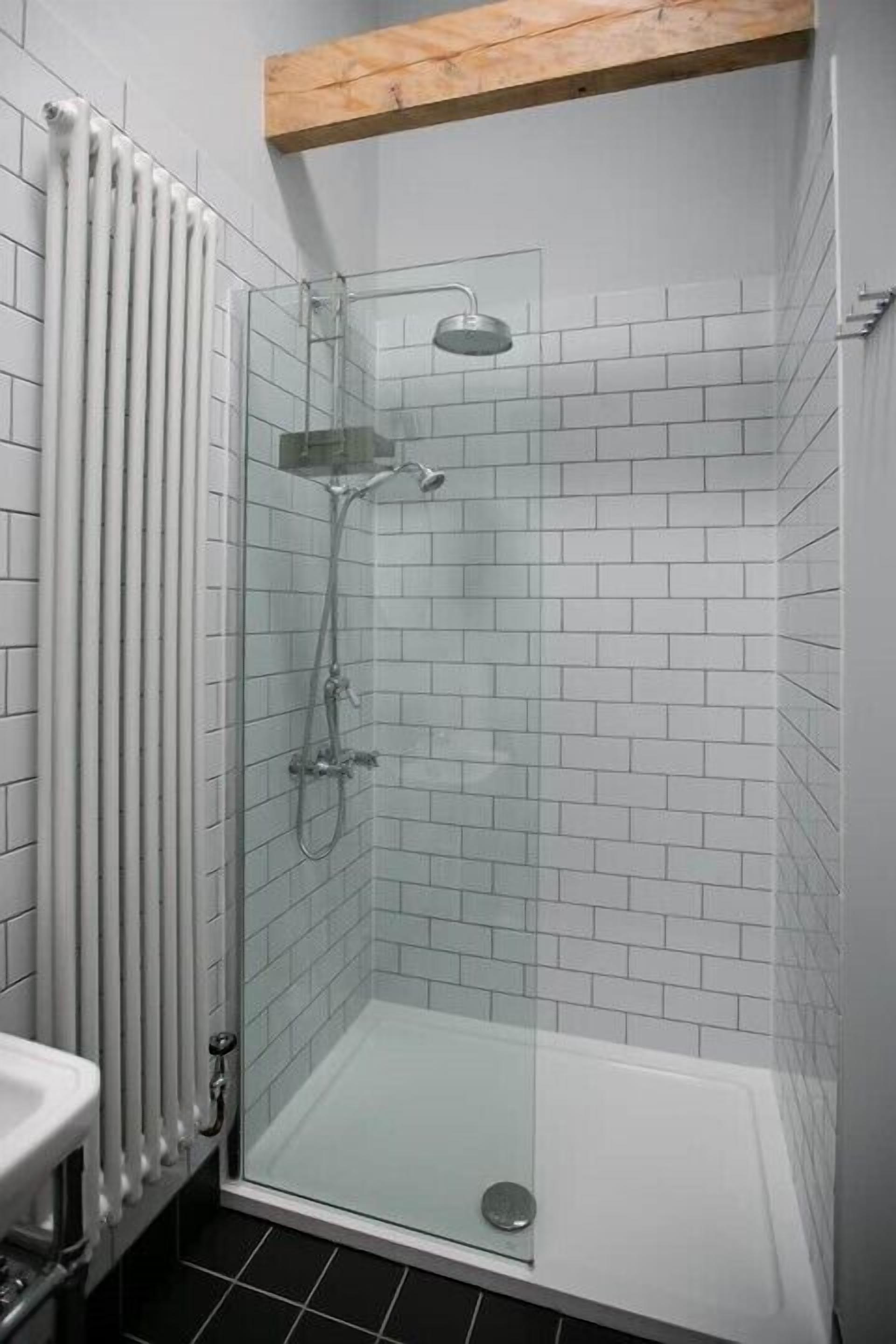 A shower with a glass enclosure, white tiled walls, and a wooden ceiling beam.