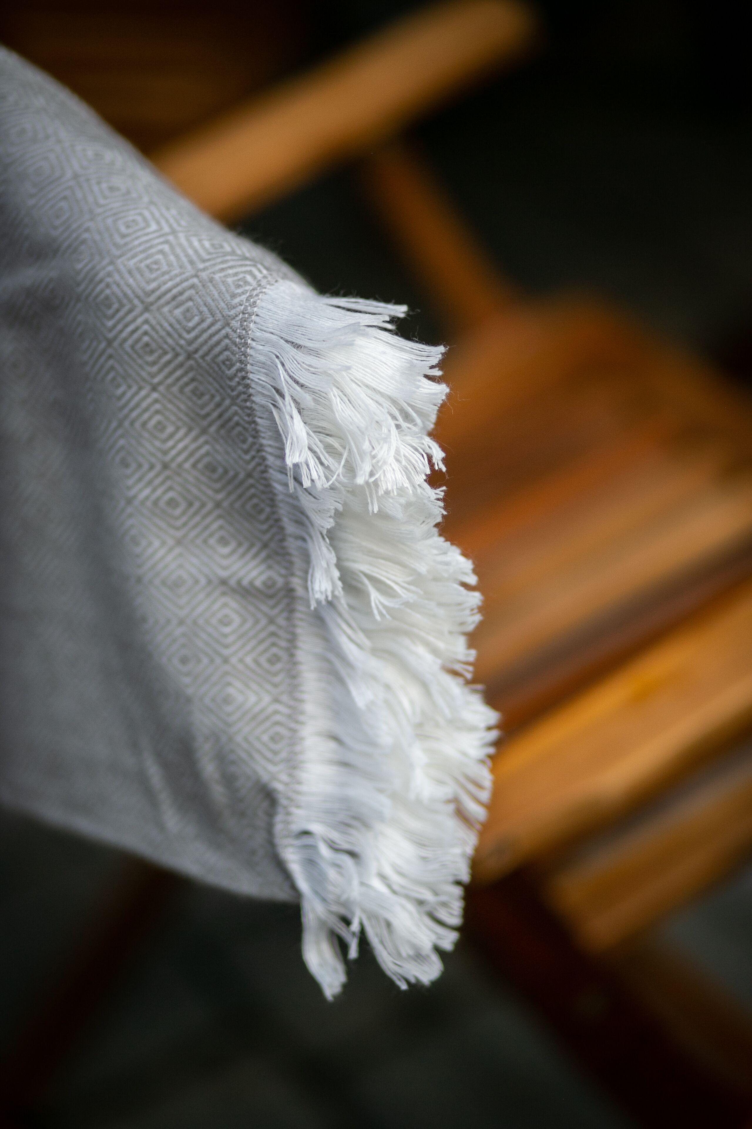 A close-up of a patterned fabric with a fringed edge, draped over a wooden chair.