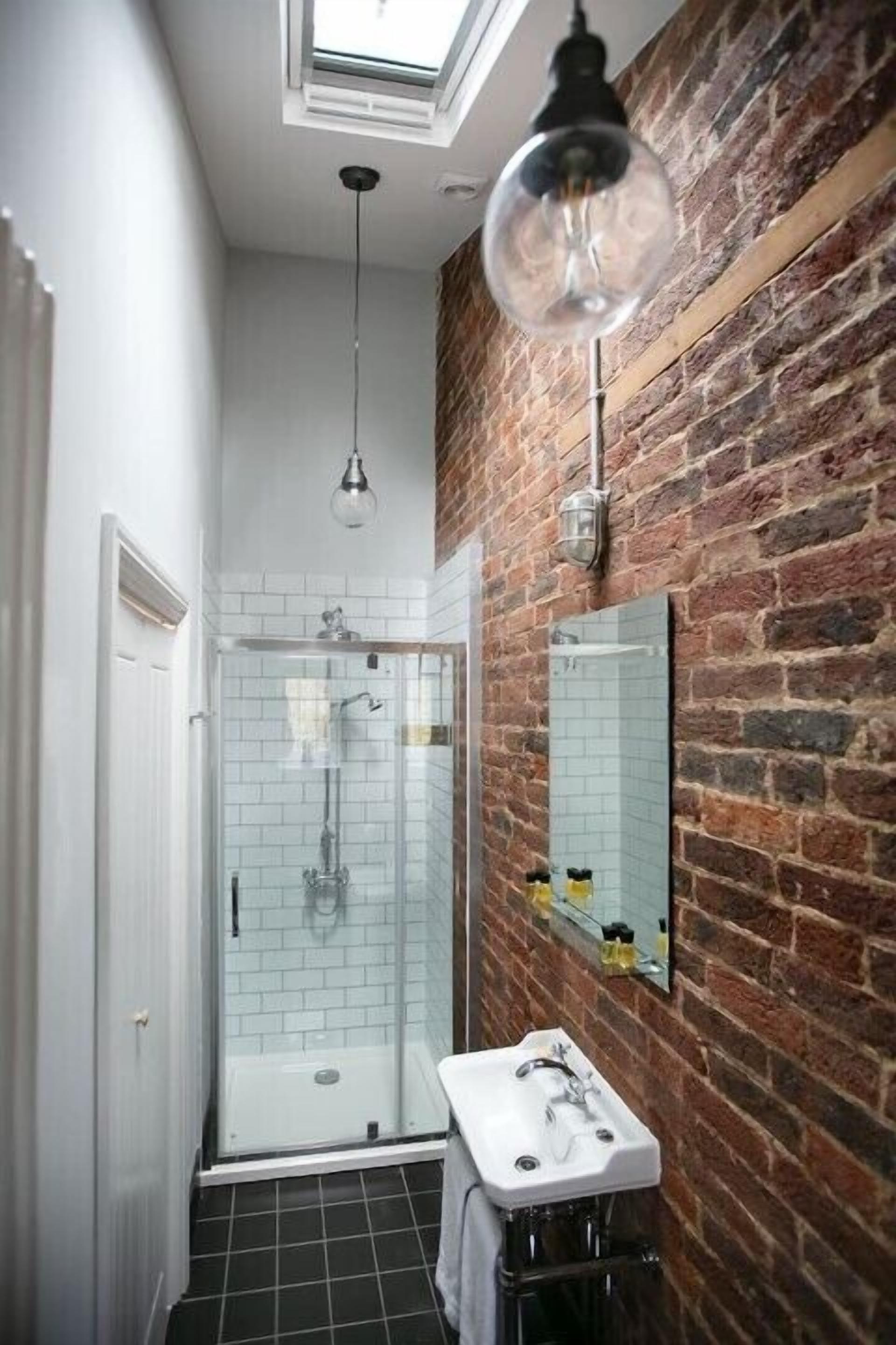 A modern bathroom with a glass shower, a white sink, and a brick wall.