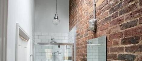 A modern bathroom with a glass shower, a white sink, and a brick wall.