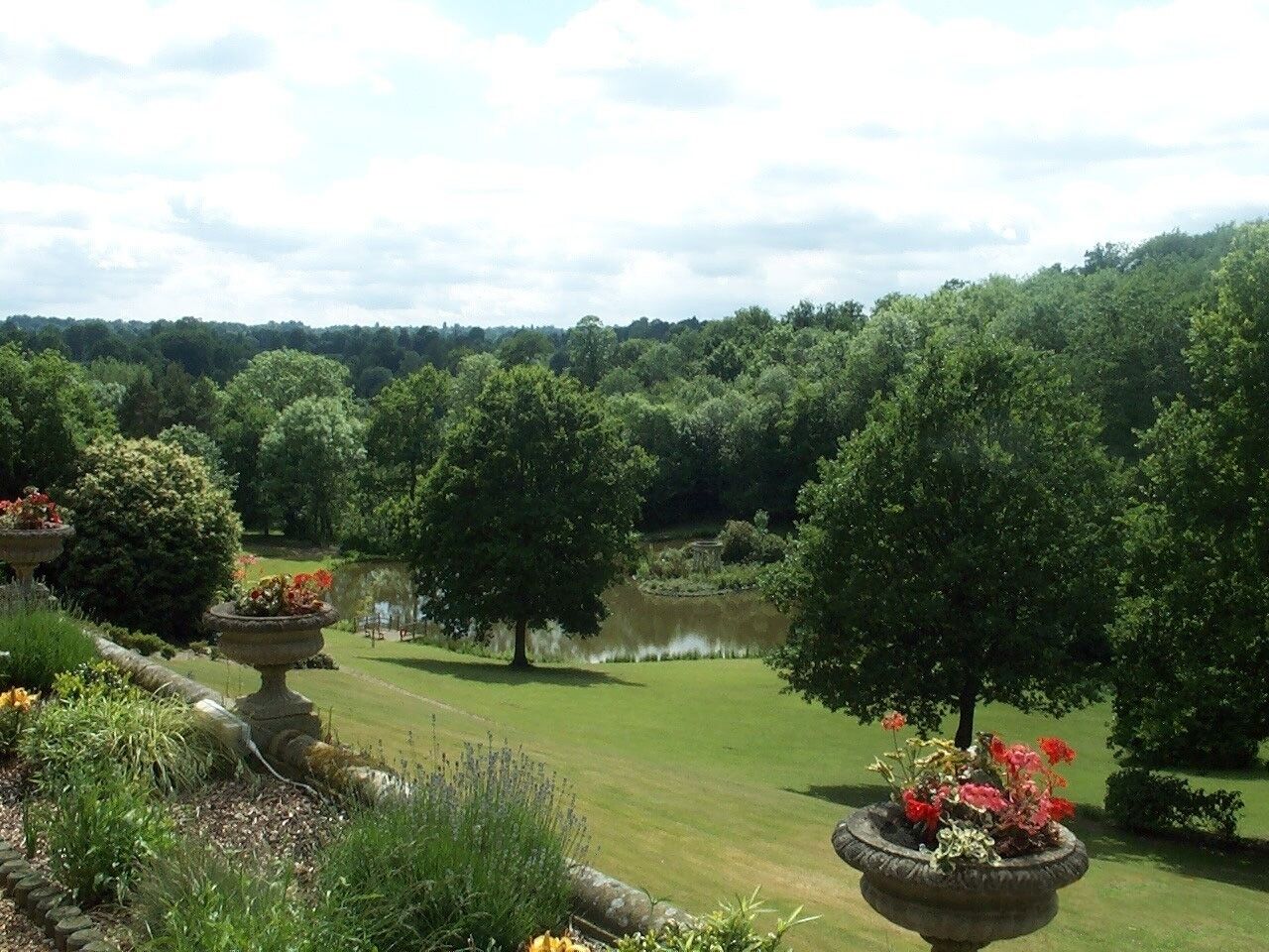 A landscaped garden with a pond, trees, and flower planters.