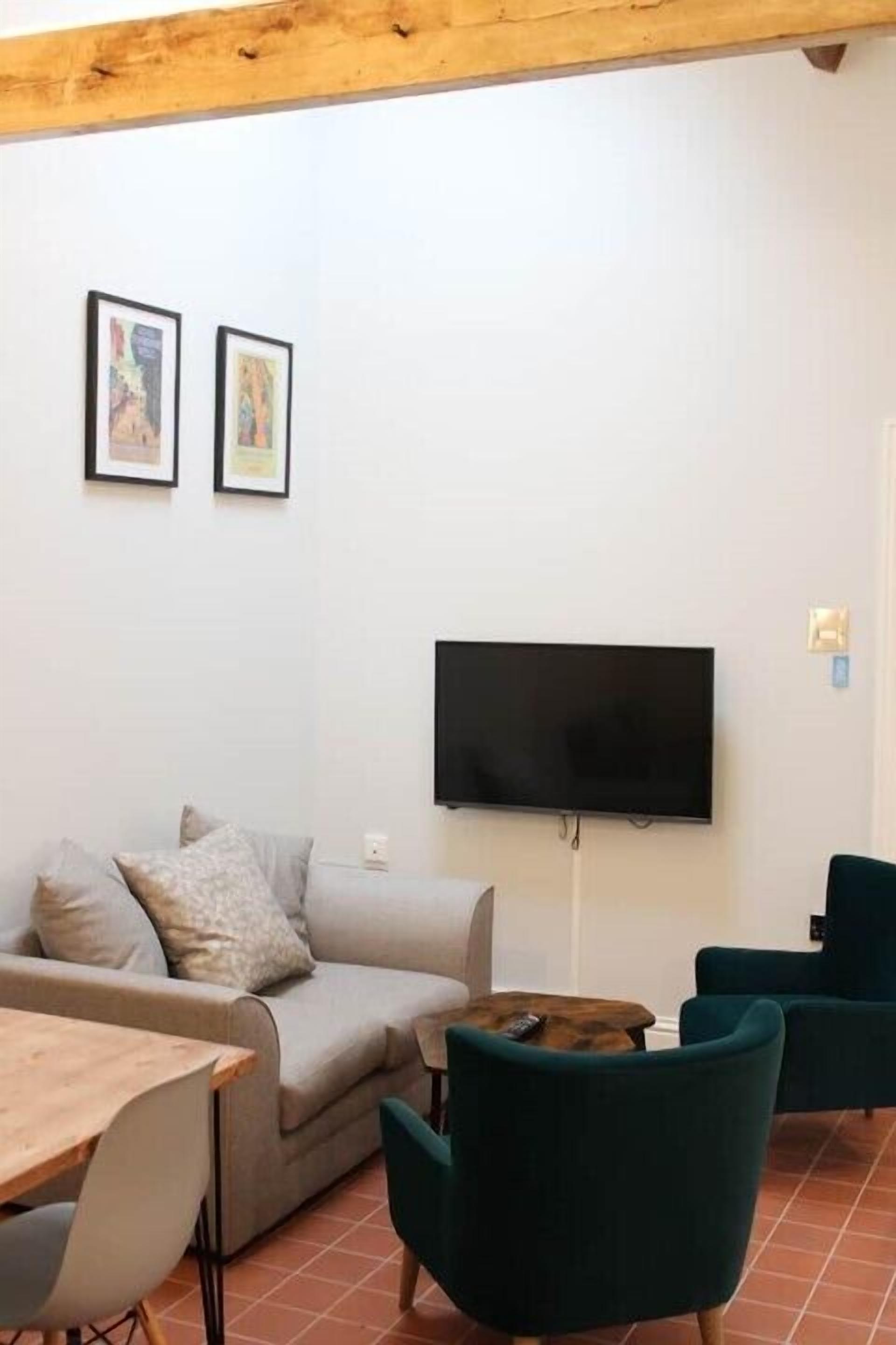 A living room with a sofa, two chairs, a table, and a TV mounted on the wall.