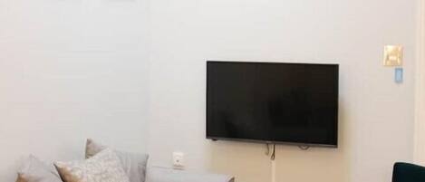 A living room with a sofa, two chairs, a table, and a TV mounted on the wall.
