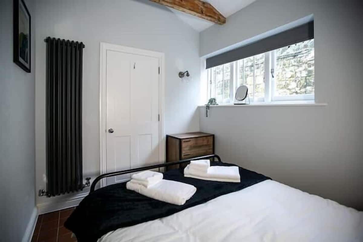 Ein Schlafzimmer mit Bett, Heizkörper, Fenster mit Blick, einer Tür und einem kleinen Nachttisch.