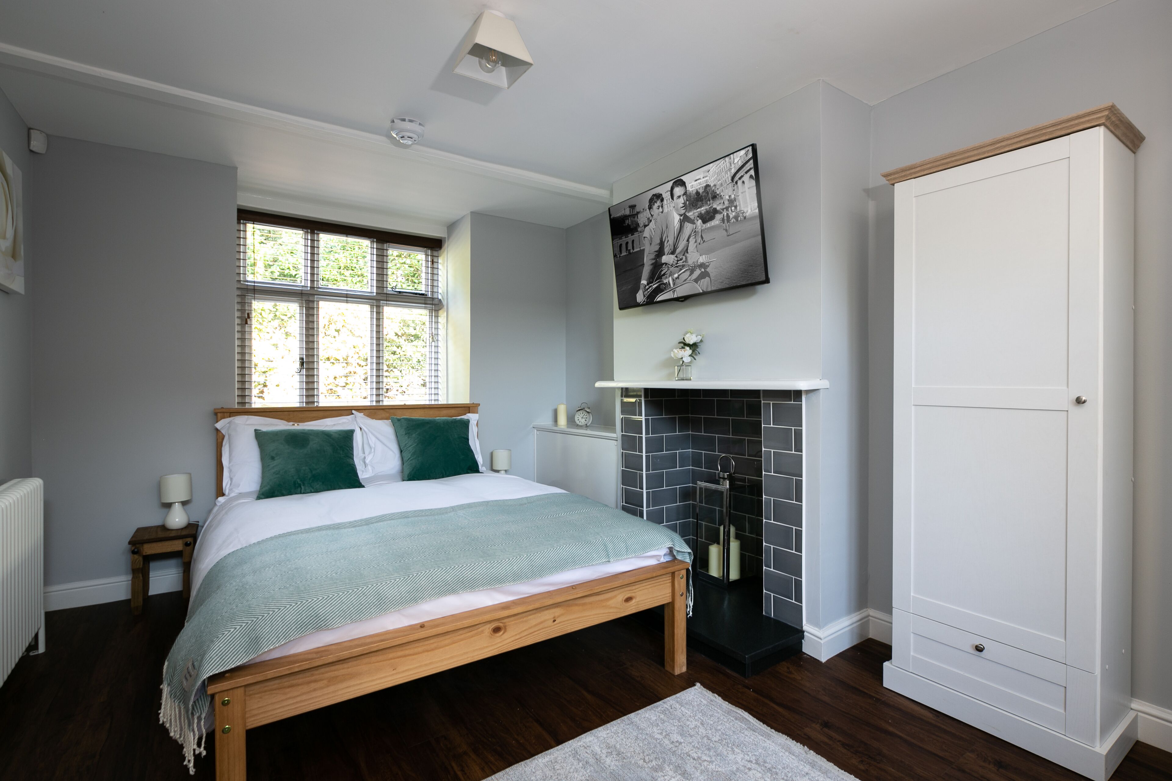 Un dormitorio con cama de madera, chimenea, armario blanco y ventana con persianas.