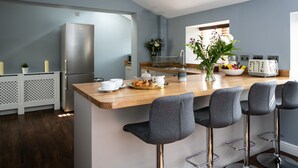 A modern kitchen with a wooden island, bar stools, a refrigerator, and a window with natural light. - Accommodation at Salomons Estate (Royal Tunbridge Wells)