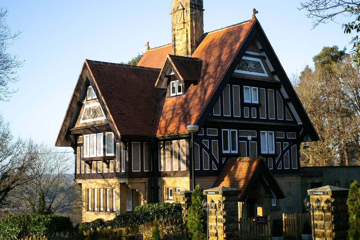Ein großes, historisches Gebäude im Tudor-Stil mit einem markanten Schornstein, Steinmauern und einem eingenommenen Eingang.