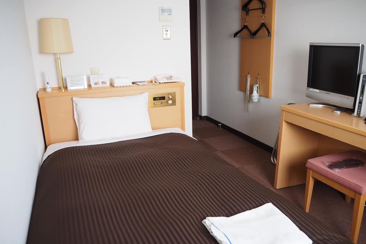 A hotel room with a bed, a desk with a computer, a telephone, and a lamp.