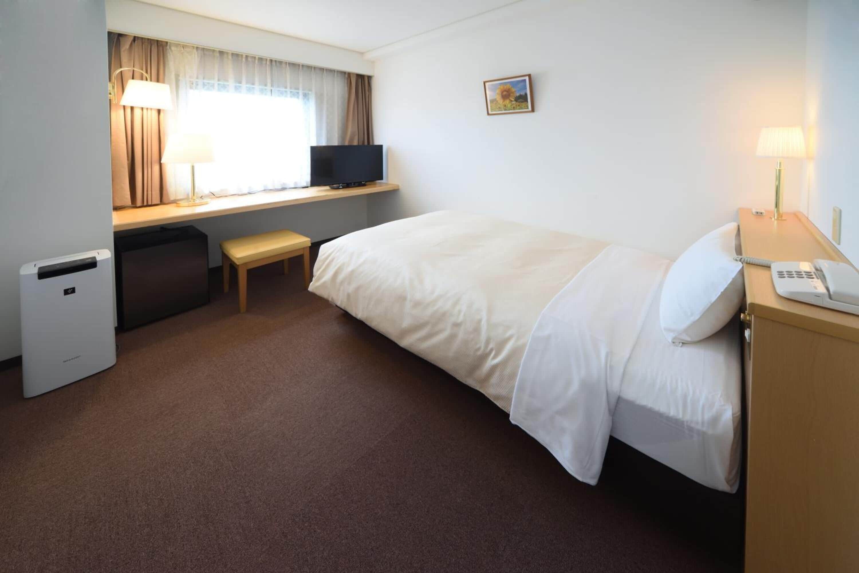 Una camera d'albergo con un letto, una scrivania con televisore, un tavolino e una lampada da comodino.