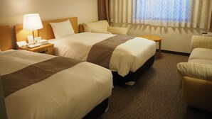 Ein Hotelzimmer mit zwei Betten, einem Nachttisch mit Lampe, einem kleinen Tisch und einem Fenster mit Vorhängen.