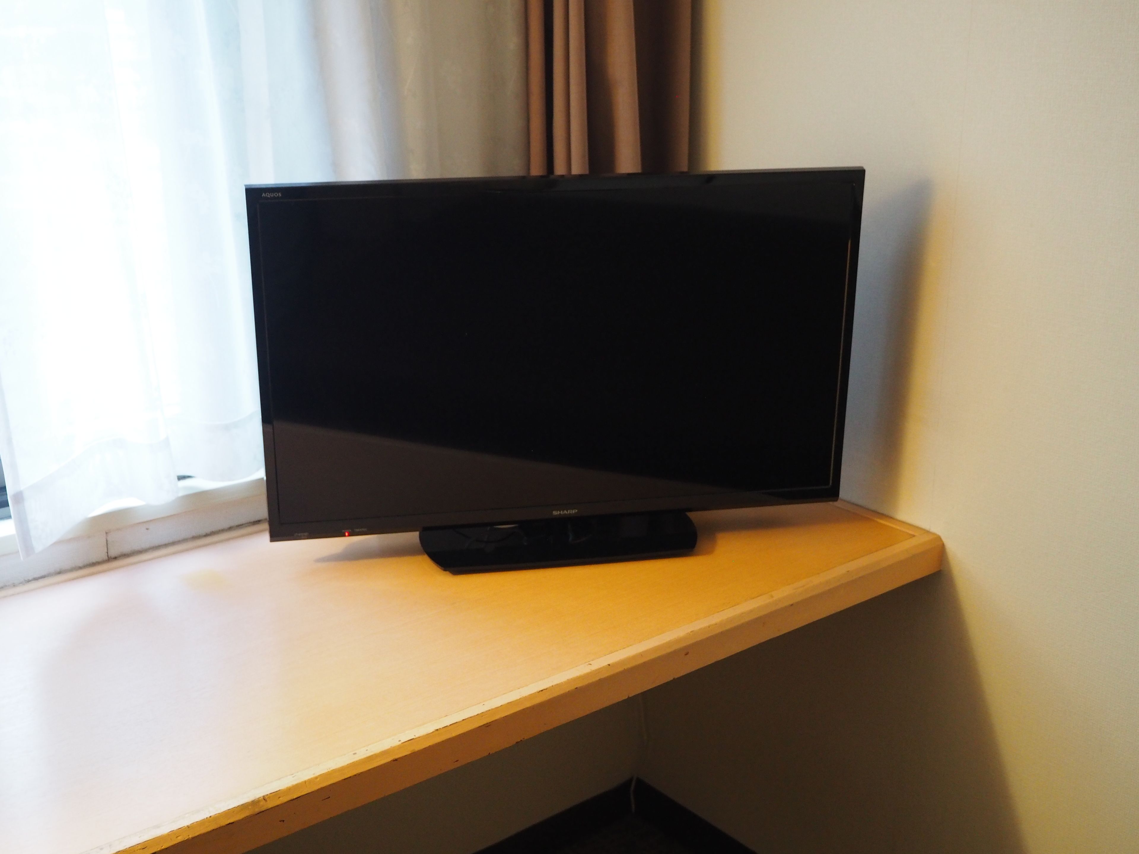 A television on a wooden desk by a window with curtains.