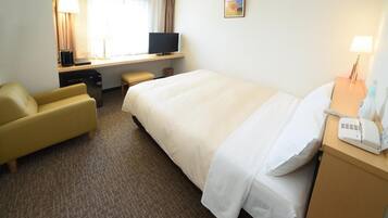 A hotel room with a bed, a desk with a computer, a chair, a lamp, and a telephone.