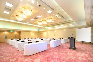 A conference room with rows of white tables, a podium, and a projection screen.