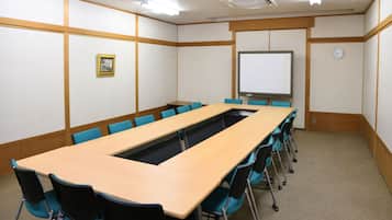 A conference room with a long table, blue chairs, a whiteboard, and a clock on the wall.