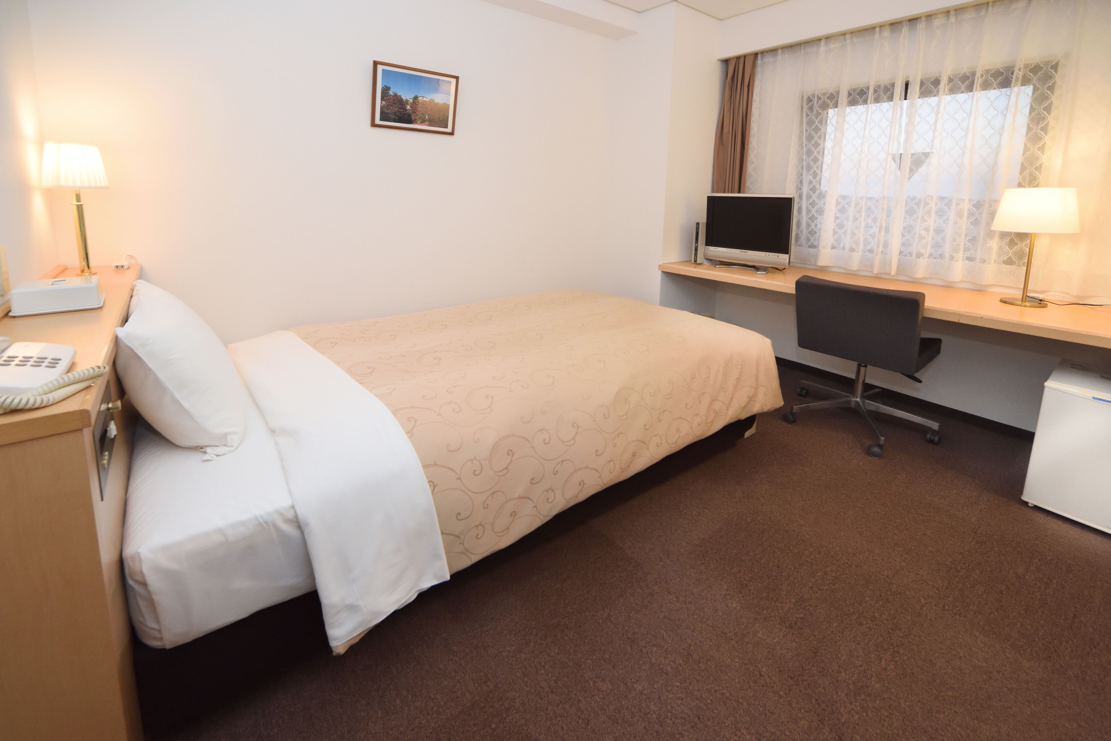A hotel room with a bed, desk, computer, and lamp.