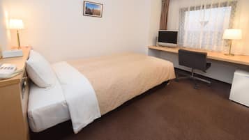 A hotel room with a bed, desk, computer, and lamp.