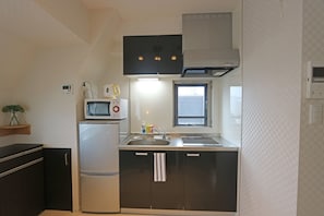 Una cocina compacta con microondas, refrigerador, lavamanos y una ventana sobre la encimera.
