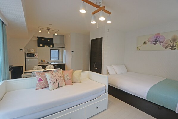 Una habitación de hotel moderna con un sofá blanco, una cama, una kitchenette y un cuadro de flores en la pared.