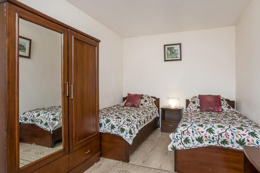 Un dormitorio con dos camas individuales, un armario y una mesita de noche con lámpara.