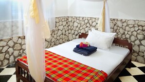A bed with a white canopy, a plaid bedspread, and a stone wall backdrop.