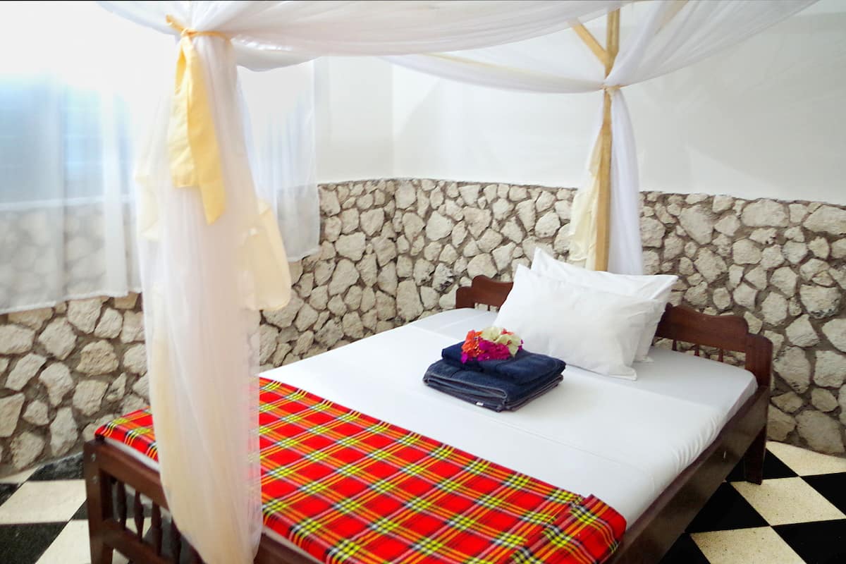 A bed with a white canopy, a plaid bedspread, and a stone wall backdrop.