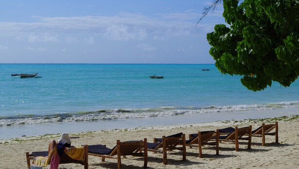 A beach with wooden lounge chairs and a person relaxing.