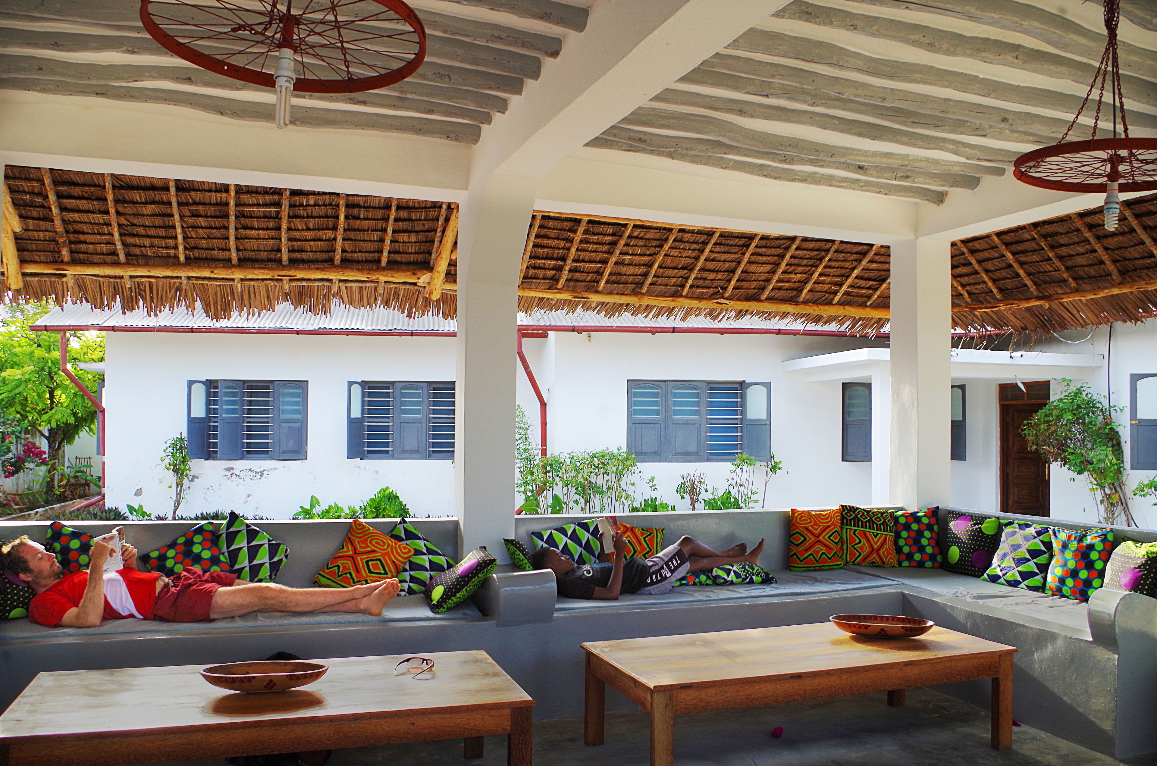 A covered outdoor seating area with a thatched roof, a wooden table, and a bowl on the table.
