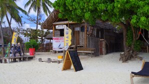 A beach hut with a reception sign, a chalkboard menu, and a wooden bench.