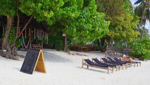 A beachside setting with a menu board, lounge chairs, and a thatched-roof structure.