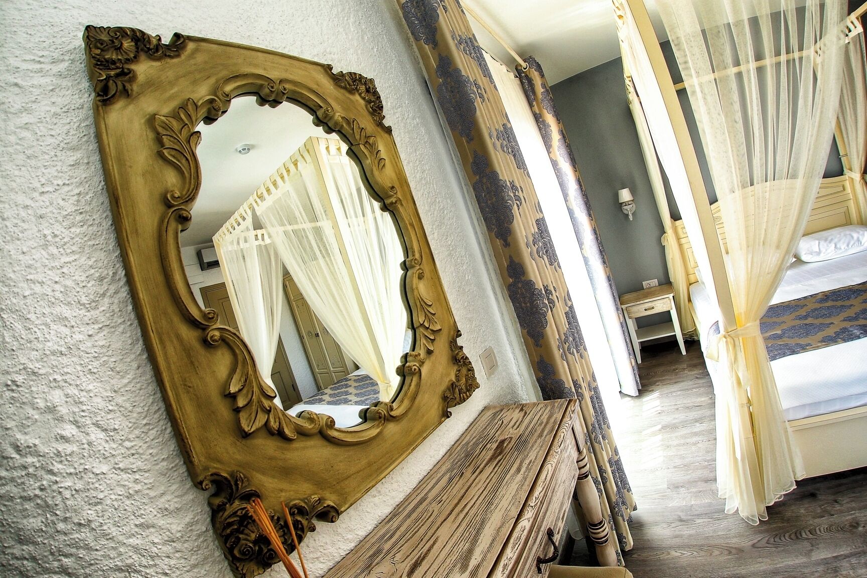 A bedroom with a large ornate mirror, a canopy bed, and a wooden bench.