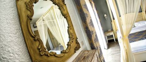 A bedroom with a large ornate mirror, a canopy bed, and a wooden bench.