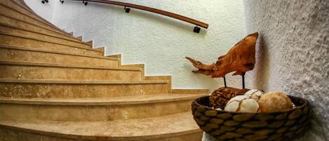 Un escalier avec une rampe en bois, une étagère fixée au mur sur laquelle se trouve un panier d’œufs, et une sculpture d’oiseau décorative.
