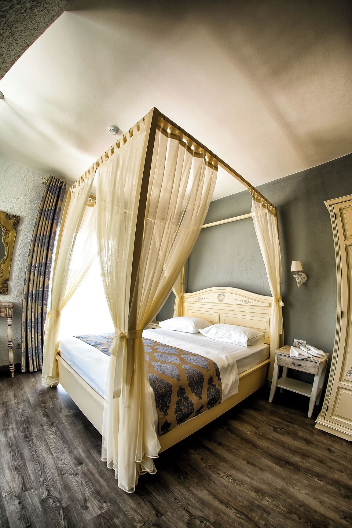 A four-poster canopy bed with a wooden headboard, a bedside table, and a mirror on the wall.