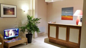 A reception area with a reception desk, a potted plant, a television, and a framed picture on the wall. - Hôtel Val De Loire (Azay-le-Rideau)