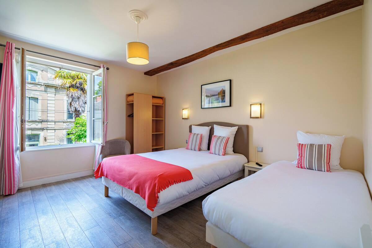 Un dormitorio con dos camas, una ventana con cortinas, techo de madera y una mesita de noche con lámpara.