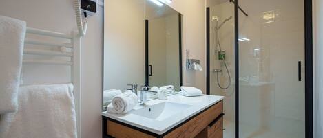 Un baño moderno con lavamanos blanco, un espejo grande y una ducha con cerramiento de vidrio.