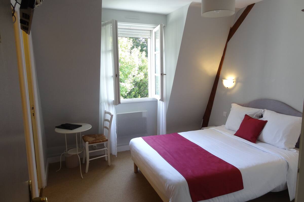 Habitación de hotel con cama, una mesita, una silla y una ventana.