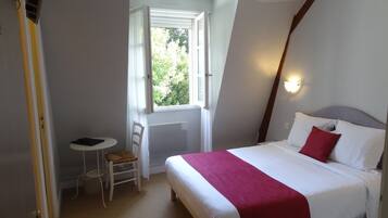 Habitación de hotel con cama, una mesita, una silla y una ventana.