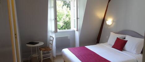 Habitación de hotel con cama, una mesita, una silla y una ventana.