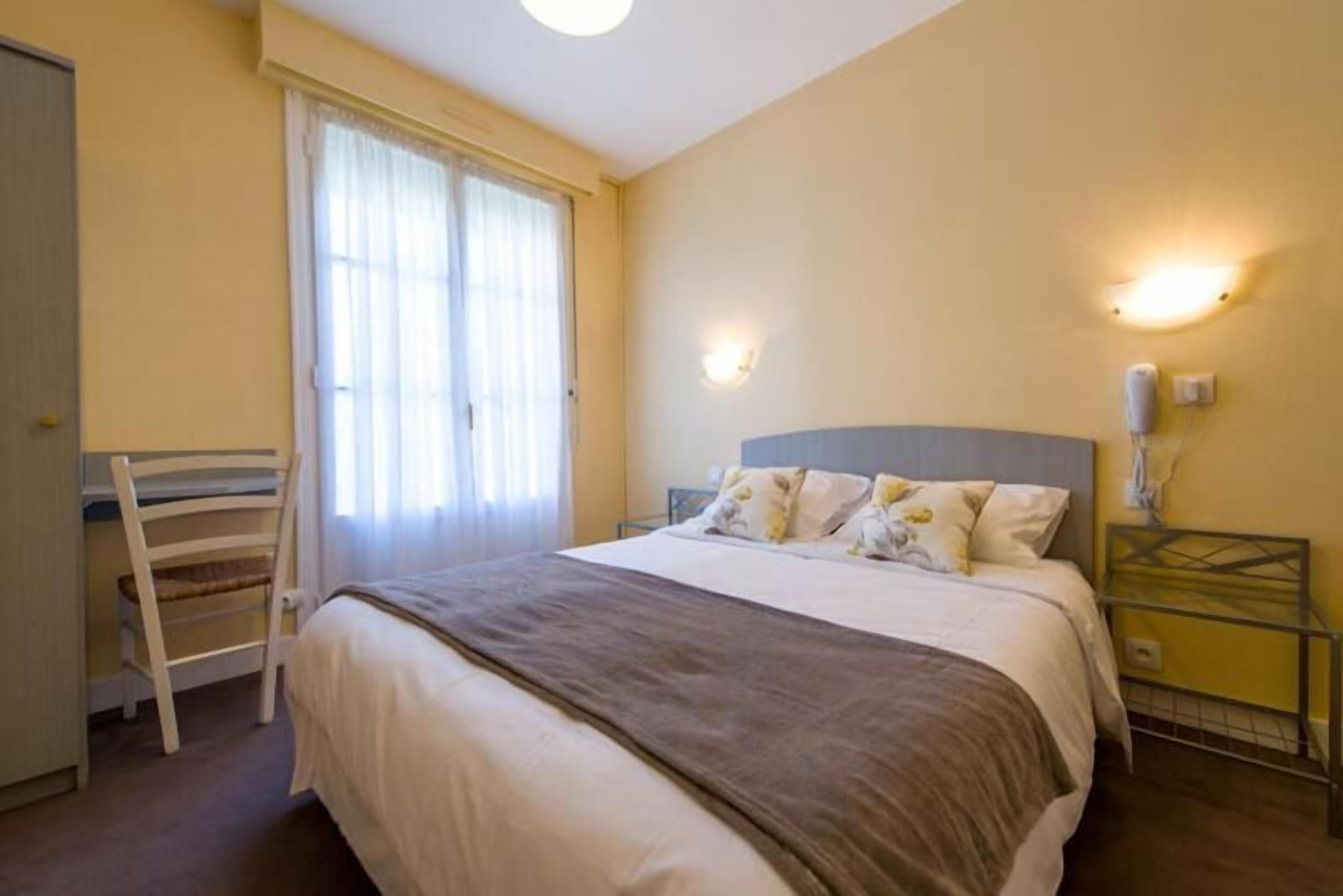 A bedroom with a bed, a chair, a desk, and a nightstand.