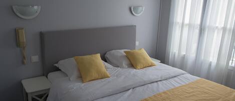 Una cama bien hecha con ropa de cama blanca y amarilla, una mesita de noche y una lámpara de pared.